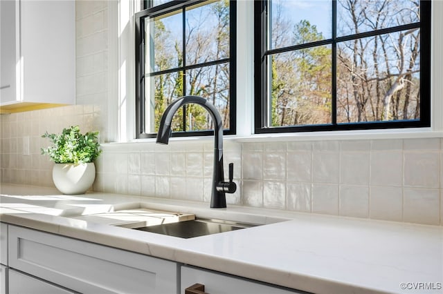 interior details featuring light stone counters, a sink, white cabinetry, and tasteful backsplash