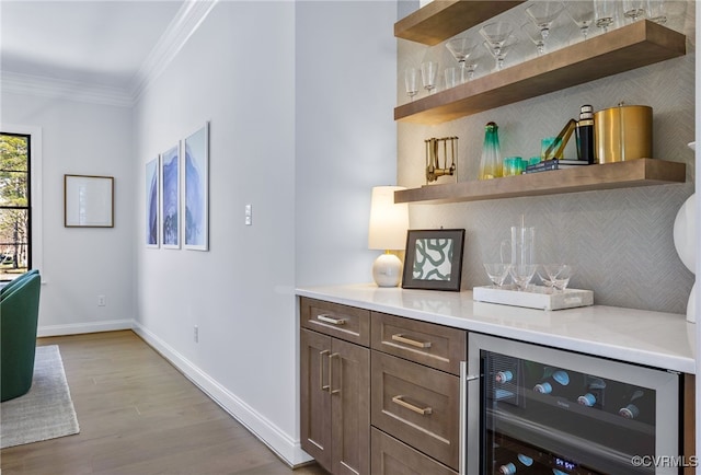 bar featuring beverage cooler, wood finished floors, ornamental molding, baseboards, and a bar