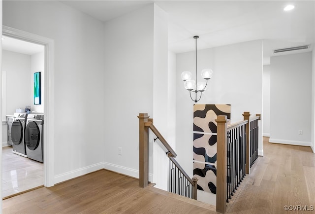 hall with an upstairs landing, visible vents, separate washer and dryer, and wood finished floors