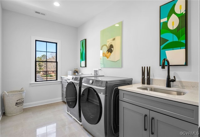 clothes washing area with cabinet space, washing machine and dryer, baseboards, visible vents, and a sink
