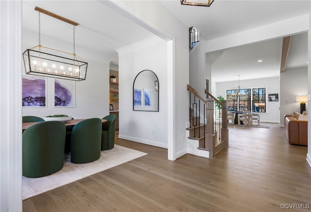 entrance foyer with stairway, a notable chandelier, crown molding, baseboards, and wood finished floors