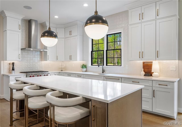 kitchen featuring a sink, light wood-type flooring, a center island, wall chimney exhaust hood, and light countertops