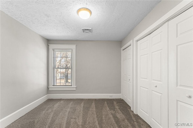 unfurnished bedroom with a textured ceiling, visible vents, two closets, carpet, and baseboards