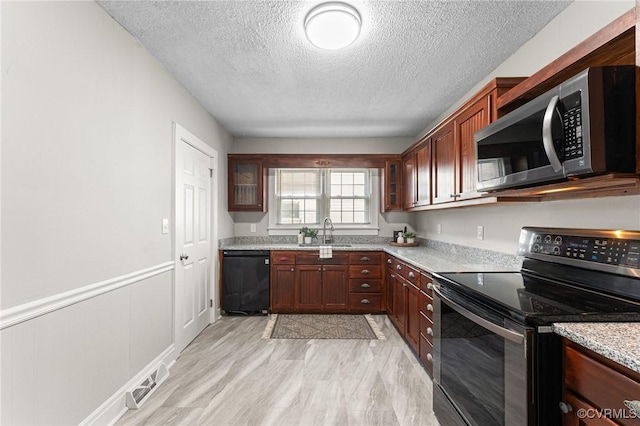 kitchen with a sink, a textured ceiling, wainscoting, stainless steel appliances, and visible vents