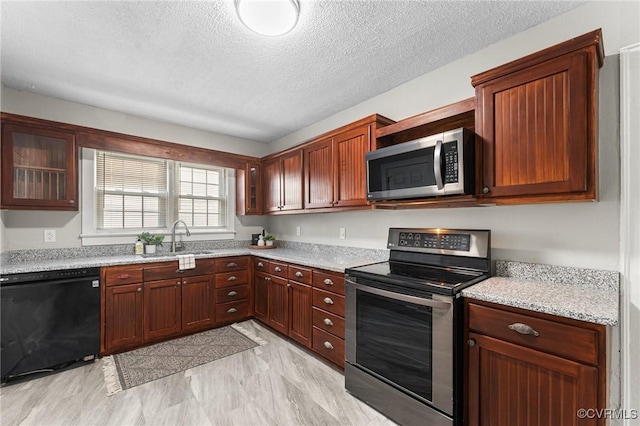 kitchen with a sink, light stone countertops, appliances with stainless steel finishes, a textured ceiling, and glass insert cabinets