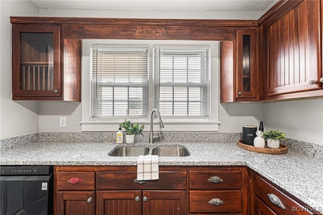 kitchen with glass insert cabinets, light stone countertops, a sink, and black dishwasher