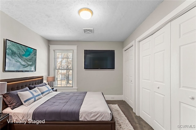 bedroom with a textured ceiling, multiple closets, baseboards, visible vents, and dark carpet