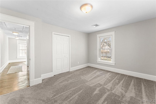 unfurnished bedroom featuring a closet, carpet flooring, visible vents, and attic access