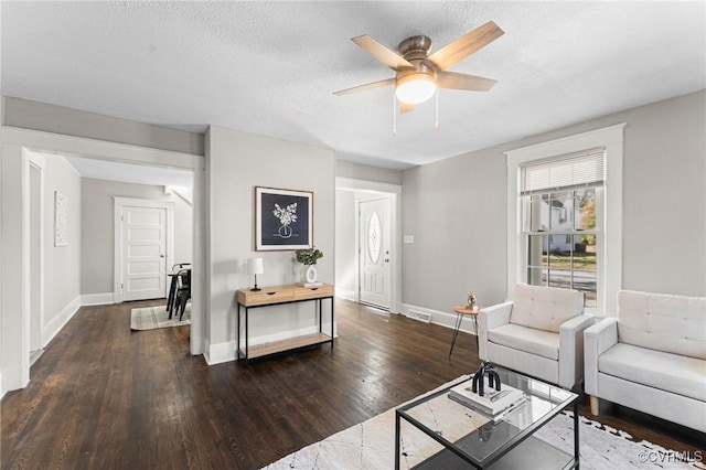 living area with baseboards, a textured ceiling, visible vents, ceiling fan, and wood finished floors