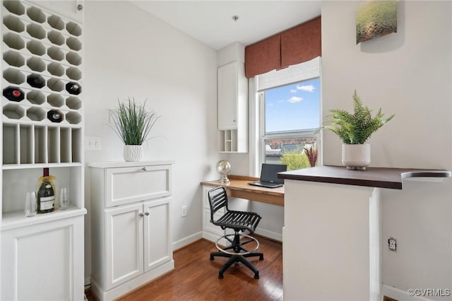 office space featuring baseboards, built in desk, and wood finished floors