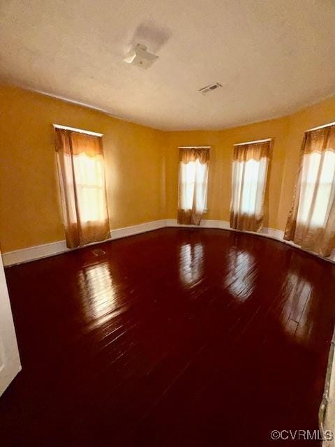 unfurnished room featuring hardwood / wood-style flooring, baseboards, a textured ceiling, and visible vents