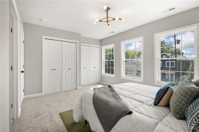 bedroom featuring multiple closets, visible vents, a chandelier, carpet, and baseboards