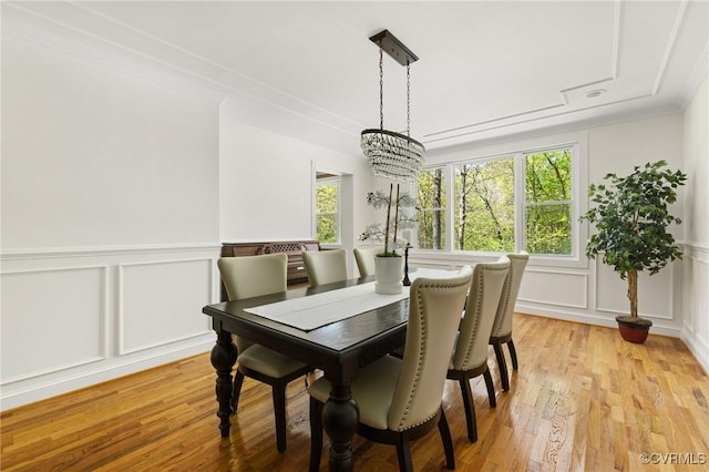 dining area with a decorative wall, a notable chandelier, wainscoting, light wood-style floors, and ornamental molding