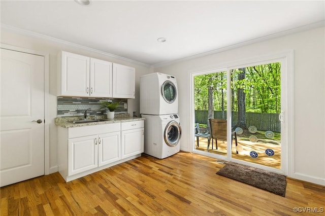 laundry room with stacked washer and clothes dryer, light wood-style flooring, crown molding, and a sink