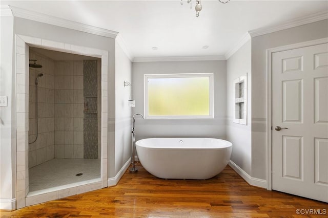 full bath featuring wood finished floors, a soaking tub, a tile shower, baseboards, and ornamental molding