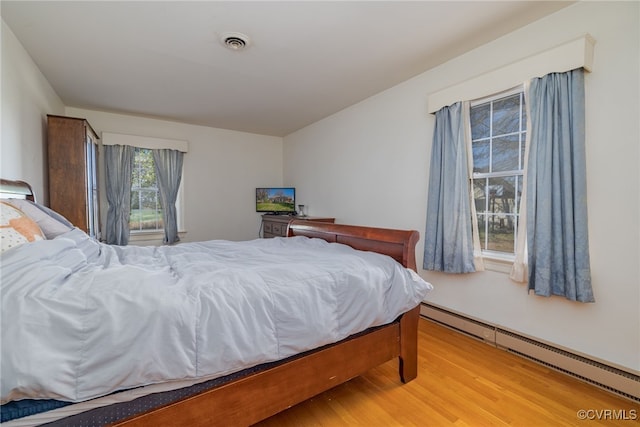 bedroom with a baseboard radiator, visible vents, and light wood-style floors