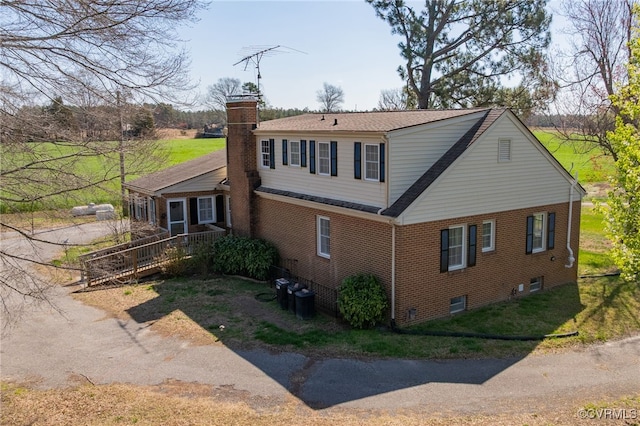 view of home's exterior with roof with shingles, a chimney, brick siding, central AC, and a yard