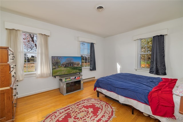 bedroom with wood finished floors, baseboards, a baseboard heating unit, and visible vents