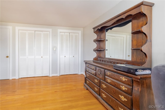 unfurnished bedroom with light wood finished floors, baseboards, and multiple closets