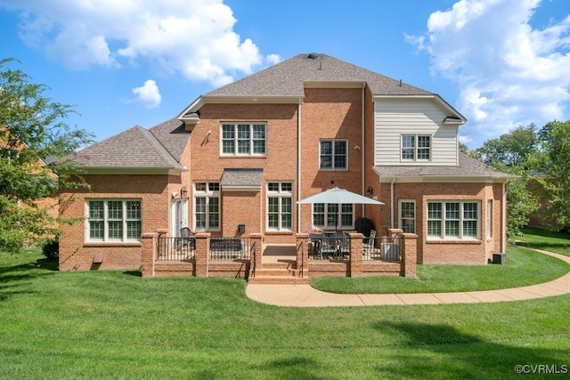 back of property with a yard, a shingled roof, brick siding, and a patio