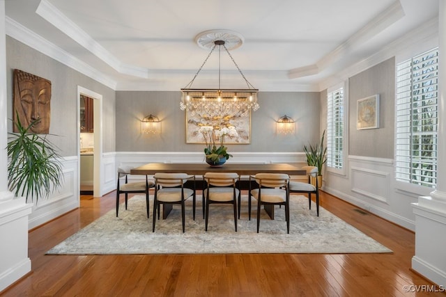 dining room with a raised ceiling, a wainscoted wall, a decorative wall, and wood finished floors