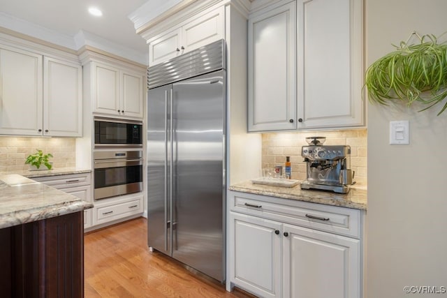 kitchen with built in appliances, white cabinetry, and backsplash