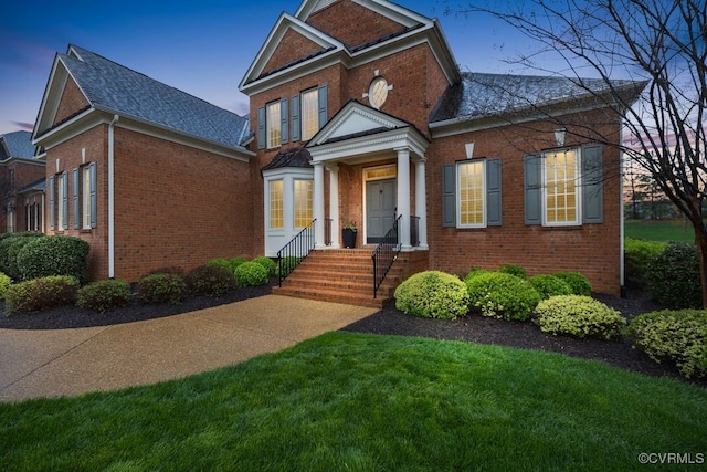 view of front of house with a shingled roof, brick siding, and a front lawn
