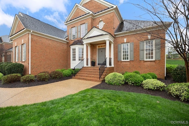 view of front facade with brick siding, a front lawn, and a shingled roof