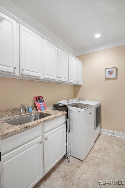 laundry area featuring baseboards, crown molding, independent washer and dryer, cabinet space, and a sink