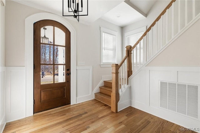 entrance foyer with a decorative wall, light wood-style flooring, visible vents, stairway, and arched walkways