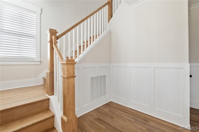 staircase featuring visible vents, wood finished floors, and a decorative wall
