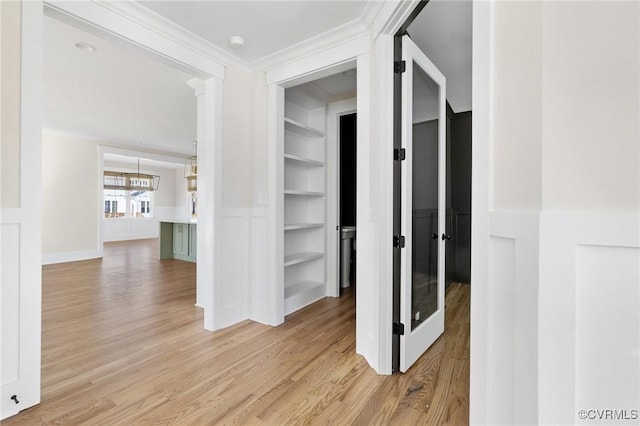 hall featuring ornamental molding, built in features, light wood finished floors, and wainscoting