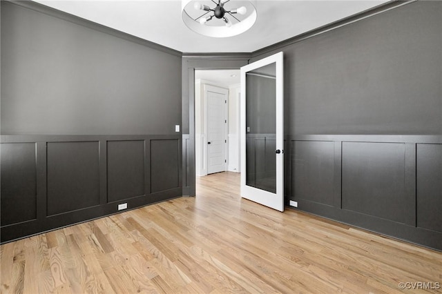 empty room with a wainscoted wall, a decorative wall, light wood-style flooring, and crown molding