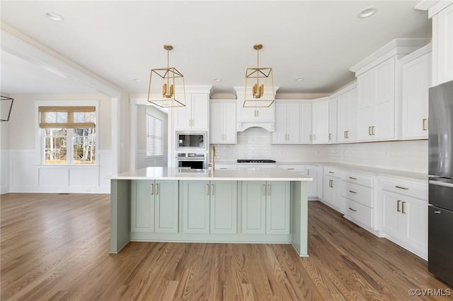 kitchen featuring an island with sink, light countertops, wood finished floors, and stainless steel appliances