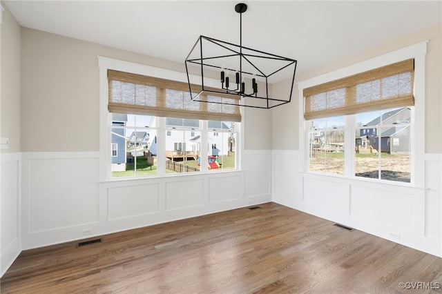 unfurnished dining area with a wainscoted wall, visible vents, a notable chandelier, and wood finished floors