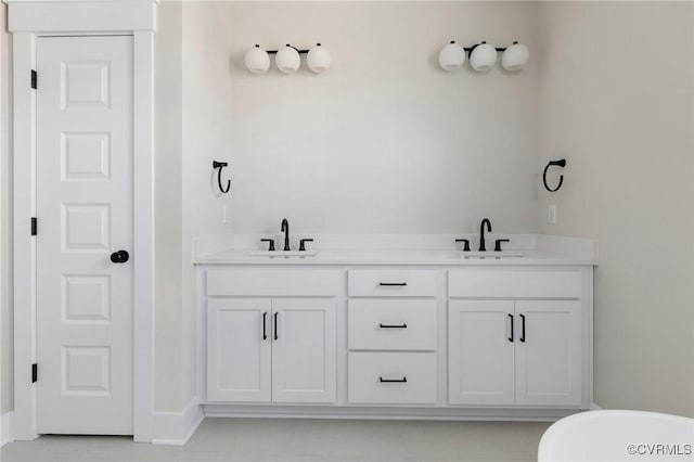 bathroom featuring double vanity, a freestanding bath, baseboards, and a sink