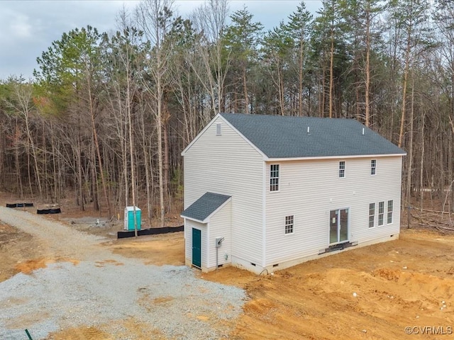 exterior space featuring crawl space, a shingled roof, and a forest view