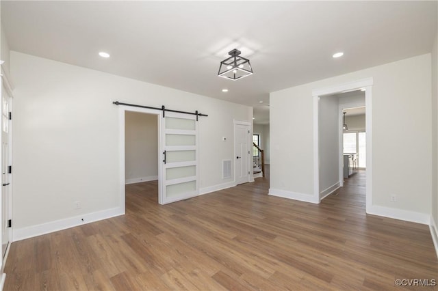 unfurnished living room with a barn door, baseboards, wood finished floors, and recessed lighting