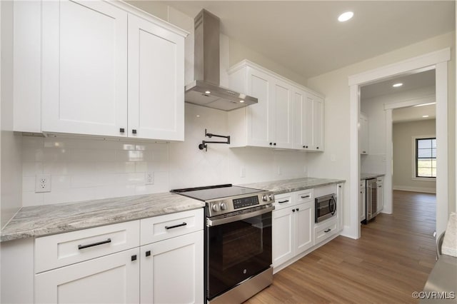 kitchen featuring wall chimney exhaust hood, stainless steel appliances, light wood-style flooring, white cabinets, and decorative backsplash