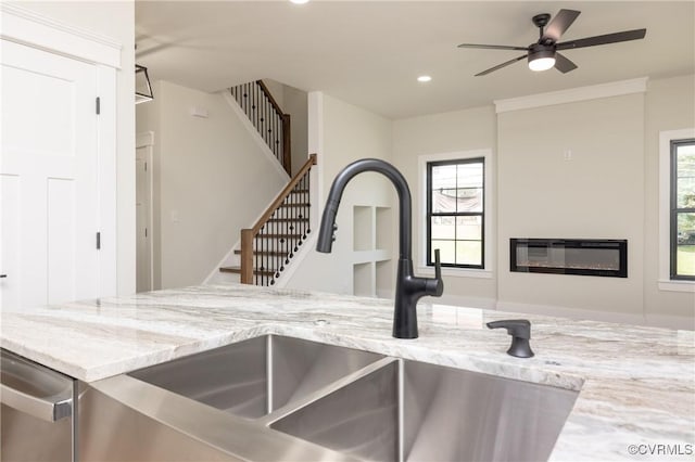 interior details featuring a sink, a glass covered fireplace, ceiling fan, light stone countertops, and recessed lighting