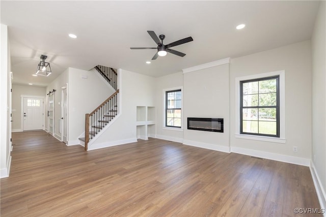 unfurnished living room with baseboards, wood finished floors, recessed lighting, and stairs
