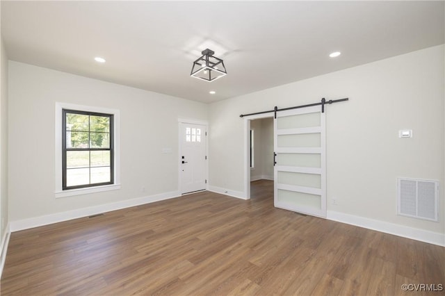 interior space featuring a barn door, wood finished floors, visible vents, and a healthy amount of sunlight