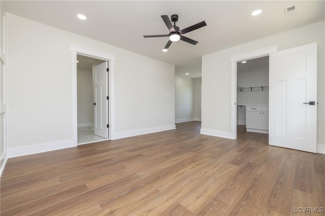 unfurnished bedroom featuring a ceiling fan, a walk in closet, light wood finished floors, baseboards, and recessed lighting