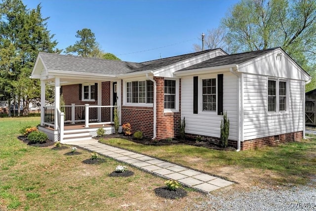 view of front of home with covered porch, a shingled roof, a front lawn, and brick siding