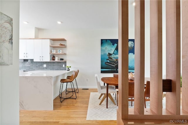 kitchen with open shelves, white cabinets, light wood finished floors, a kitchen bar, and backsplash