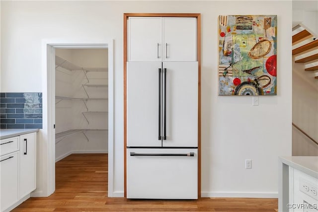 kitchen with white built in fridge, light wood finished floors, white cabinetry, and light countertops