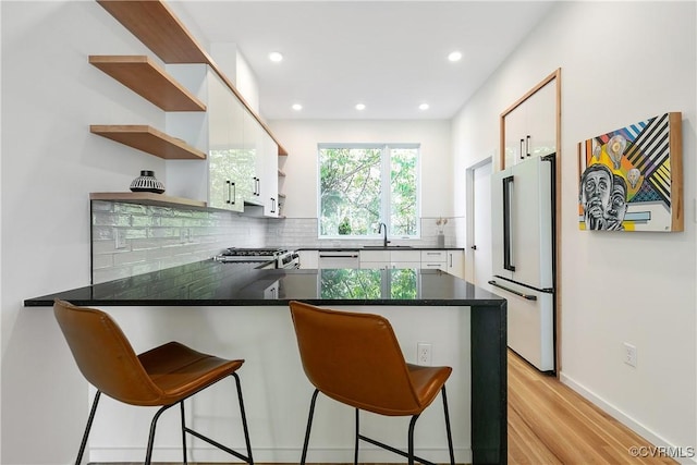 kitchen with open shelves, backsplash, freestanding refrigerator, a peninsula, and white cabinetry