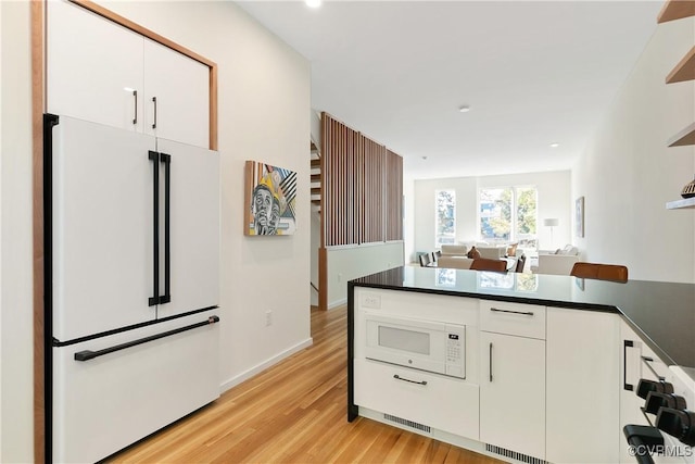 kitchen with light wood-type flooring, dark countertops, white appliances, and white cabinets