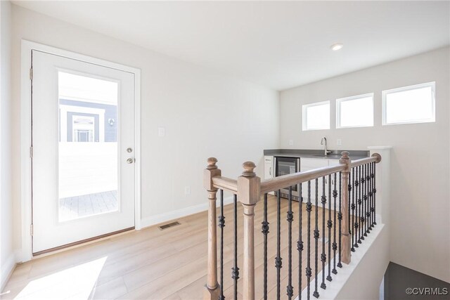 corridor featuring visible vents, a sink, beverage cooler, an upstairs landing, and light wood finished floors