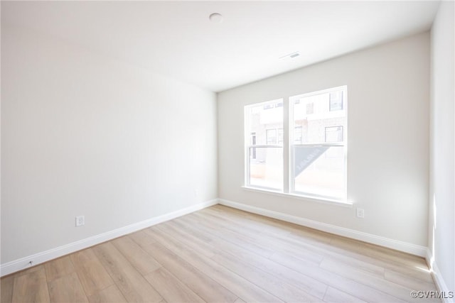 spare room with light wood finished floors, visible vents, and baseboards